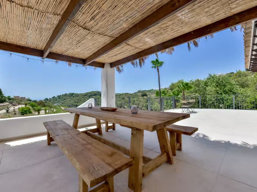 Überdachte Terrasse mit langem Holztisch und Blick über die Hügel