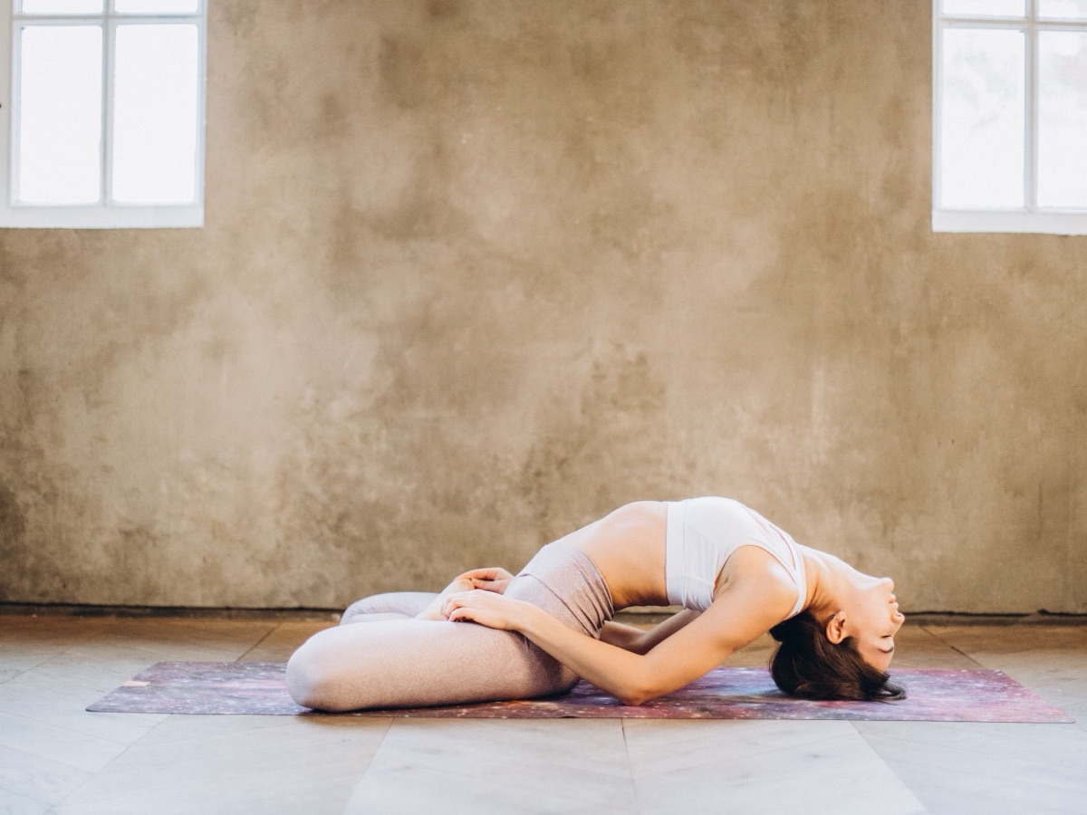 Frau in einer Yoga-Rückbeuge auf der Matte in einem lichten Raum